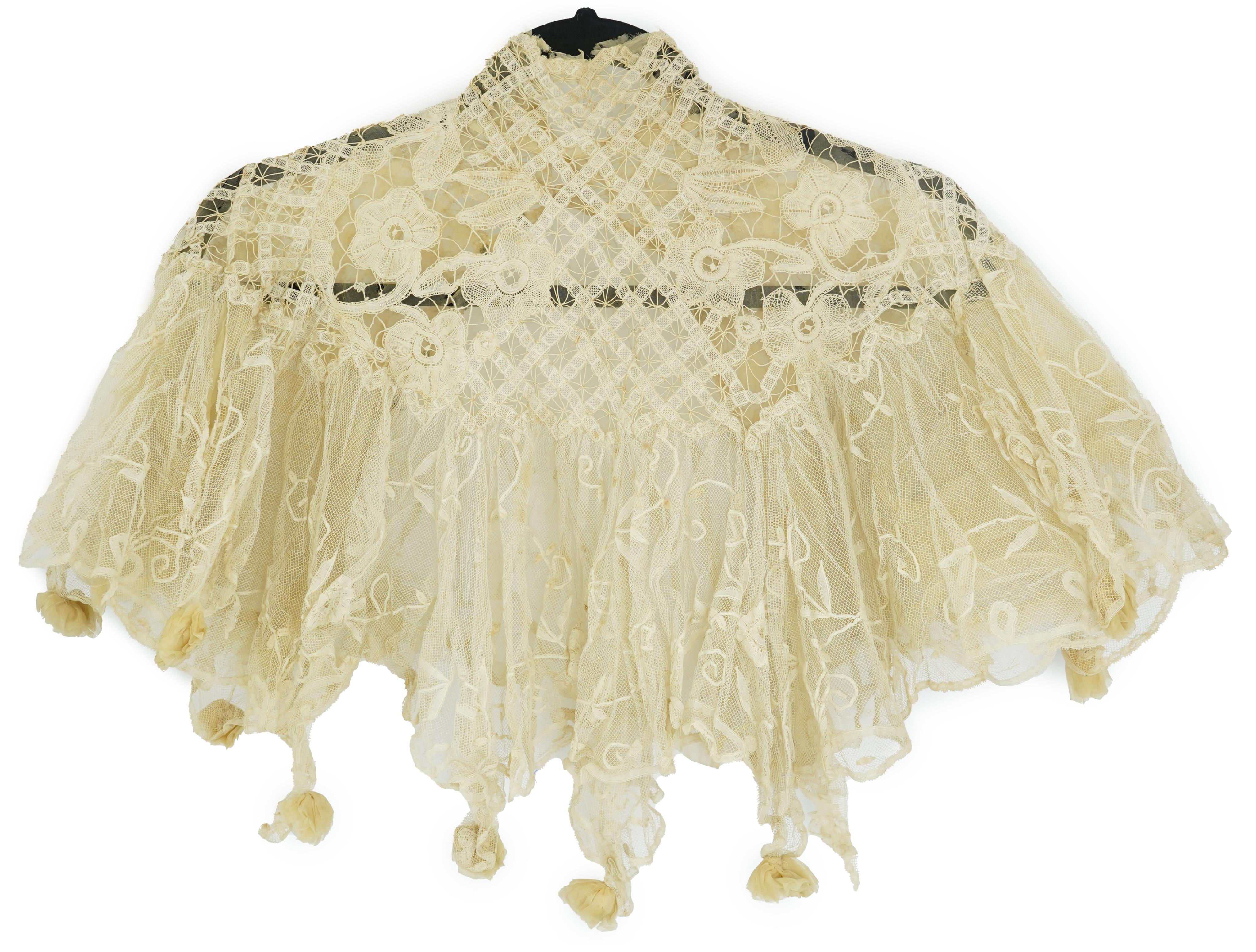 An Edwardian high collared cream tape lace wedding over blouse, made with a deep net frill and cream chiffon rose detail hanging from lower edge, top of collar to rose detail at the front 46cm. Condition - fine silk chif